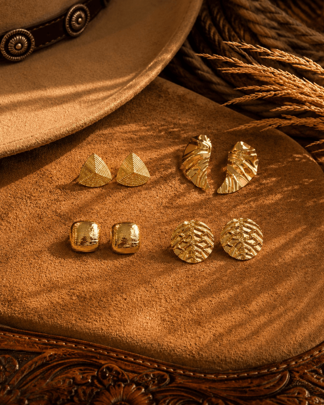 Gold earrings on suede with a western hat